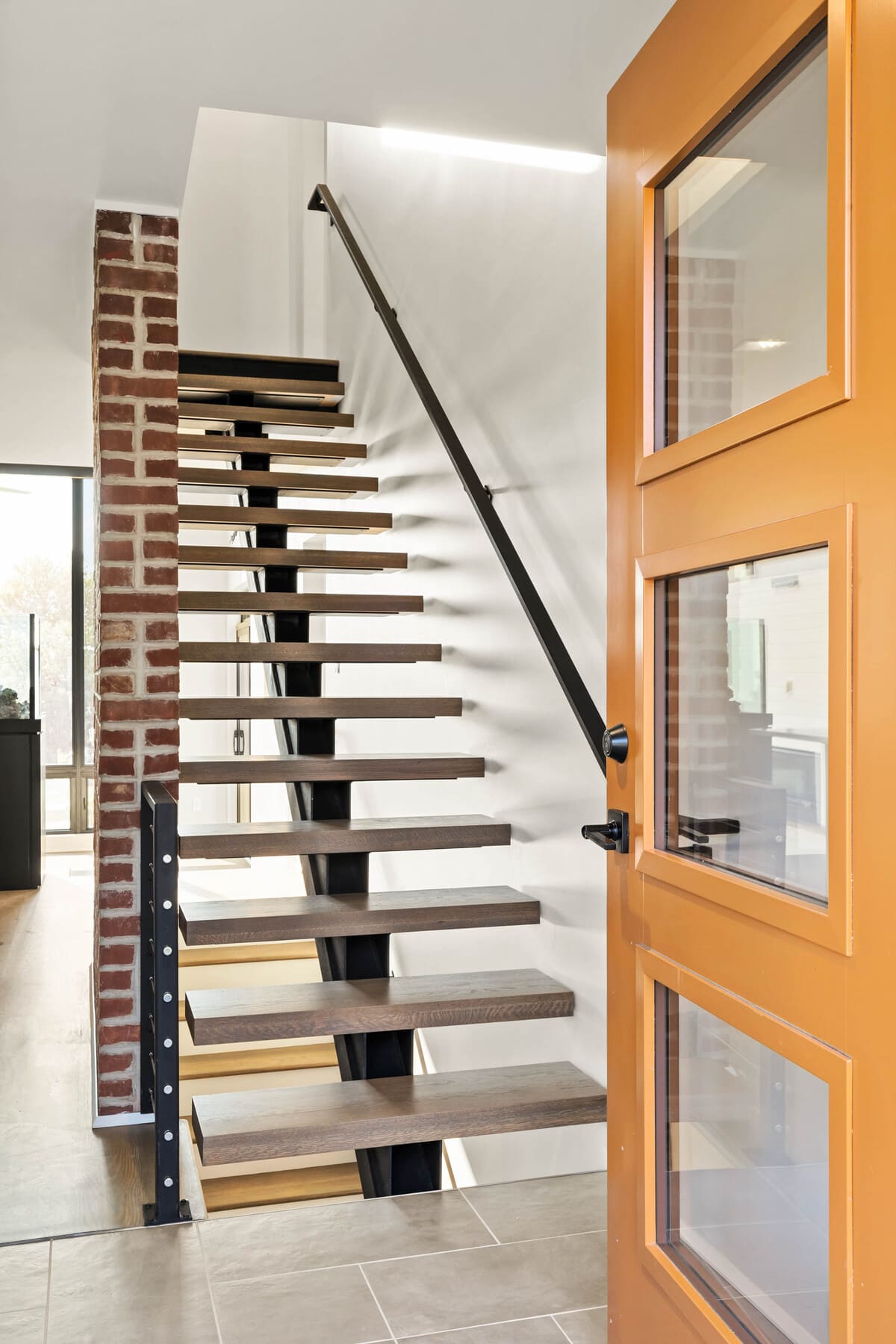 Orange door opening to staircase in foyer of Delaware custom home with orange modern door